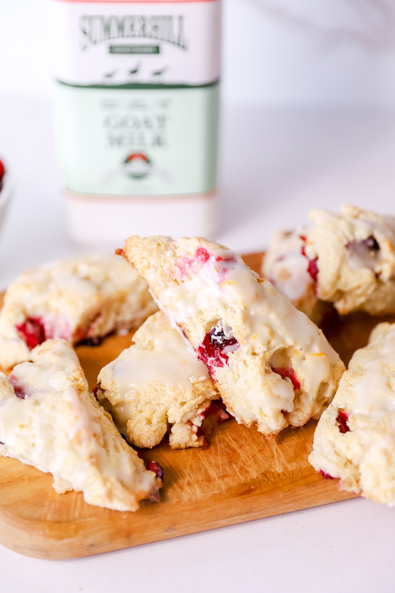 a pile of cranberry orange scones sits on a wooden cutting board. A bottle of Summerhill Goat Milk sits in the background.