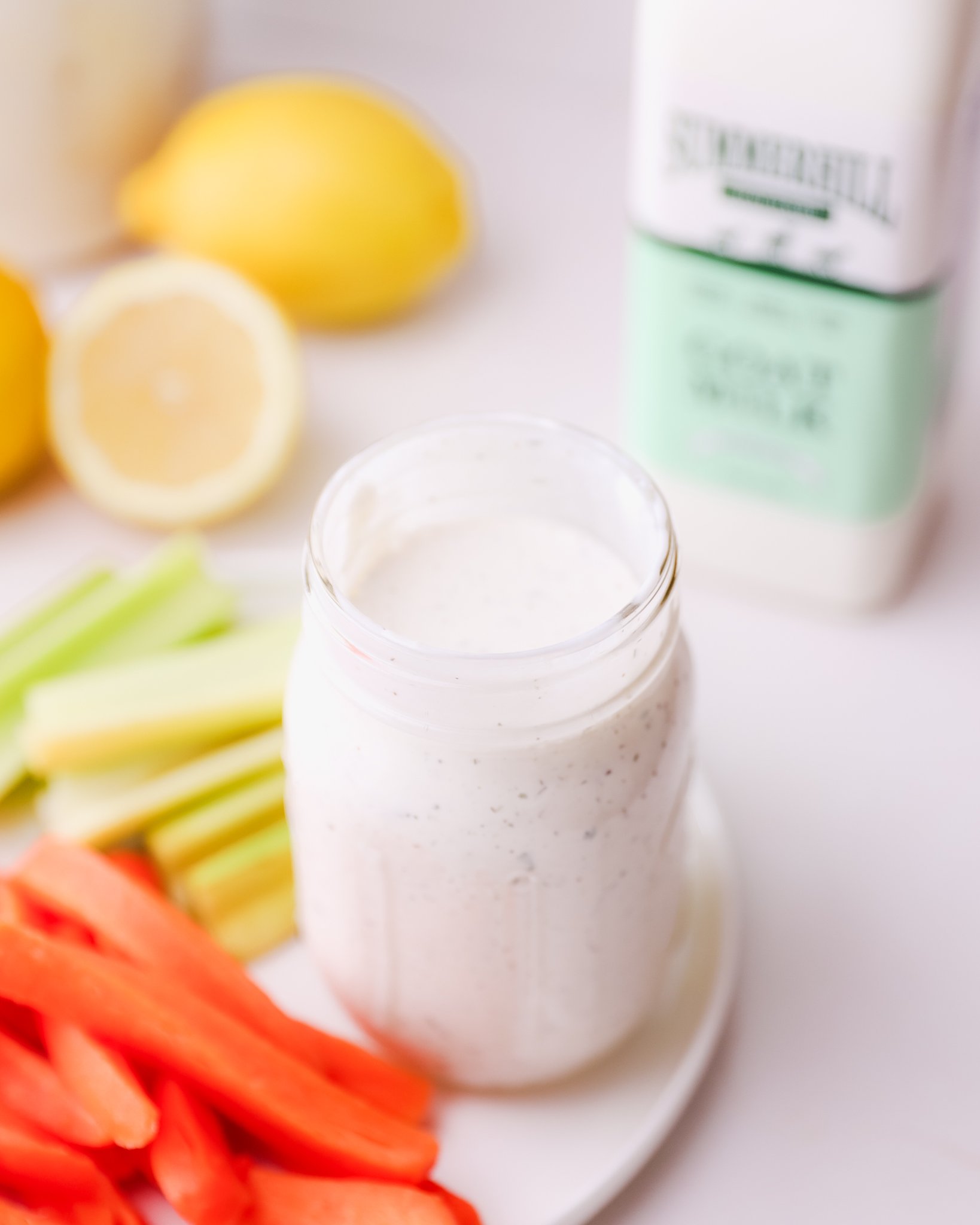 a circular white plate with veggie slices and a glass mason jar of ranch dressing sit in the bottom left corner. A bottle of Summerhill goat milk sits in the back right corner.