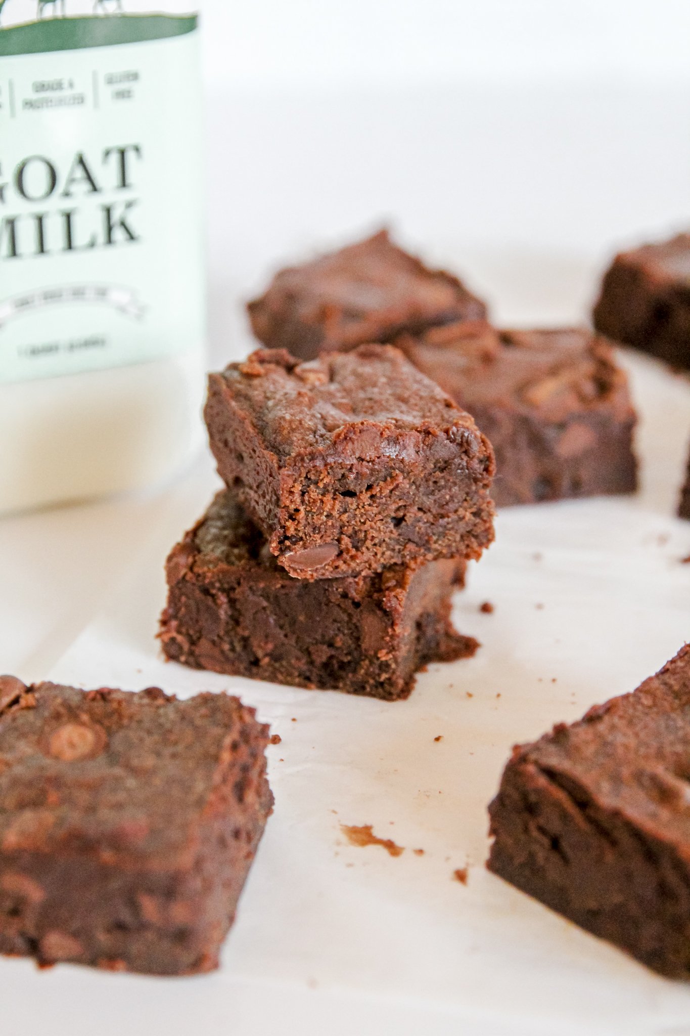 Brownies and Summerhill goat milk. Two brownies are in the foreground on either side of the photo. The center features 2 stacked brownies. In the background there is a bottle of Summerhill Goat Milk on the left, and 3 brownies on the right.