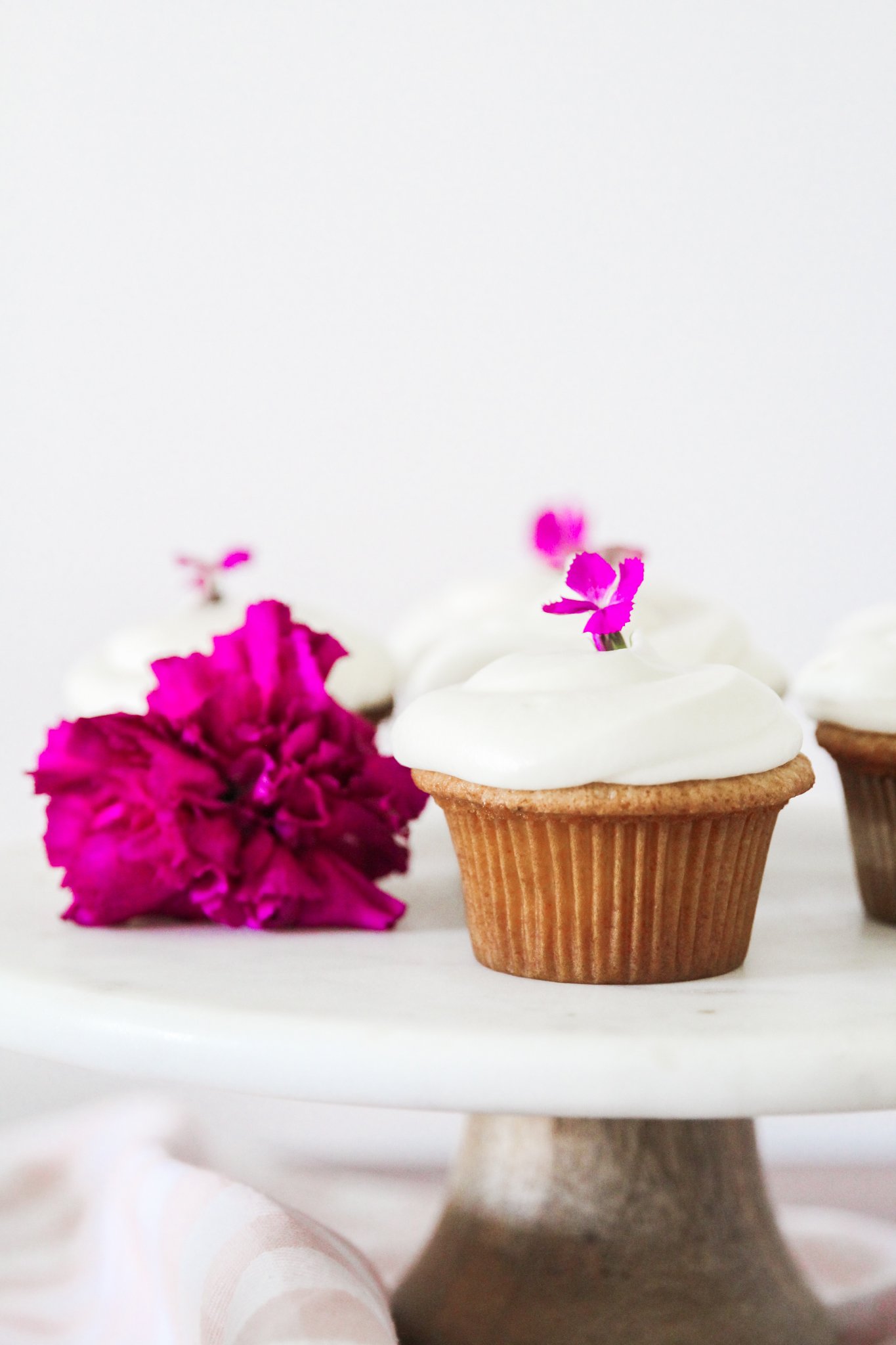 frosted honey cupcake in foreground, 2 in background. decorated with pink flowers