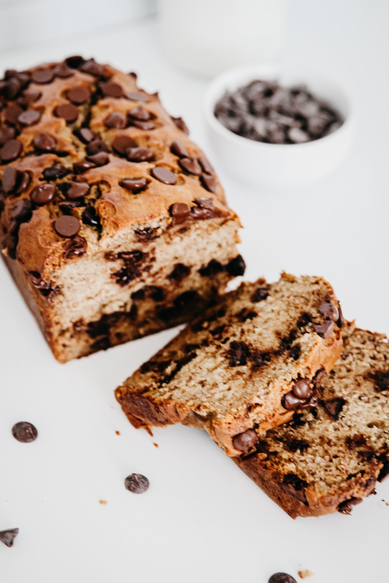 sliced chocolate chip banana bread in foreground, with ramekin of chocolate chips in background