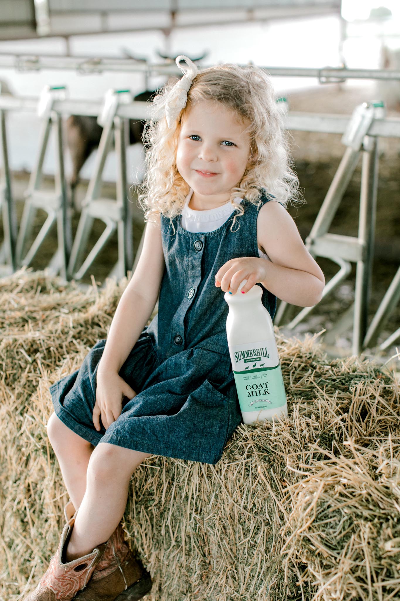 Young girl sitting on hay bale with bottle of goat milk